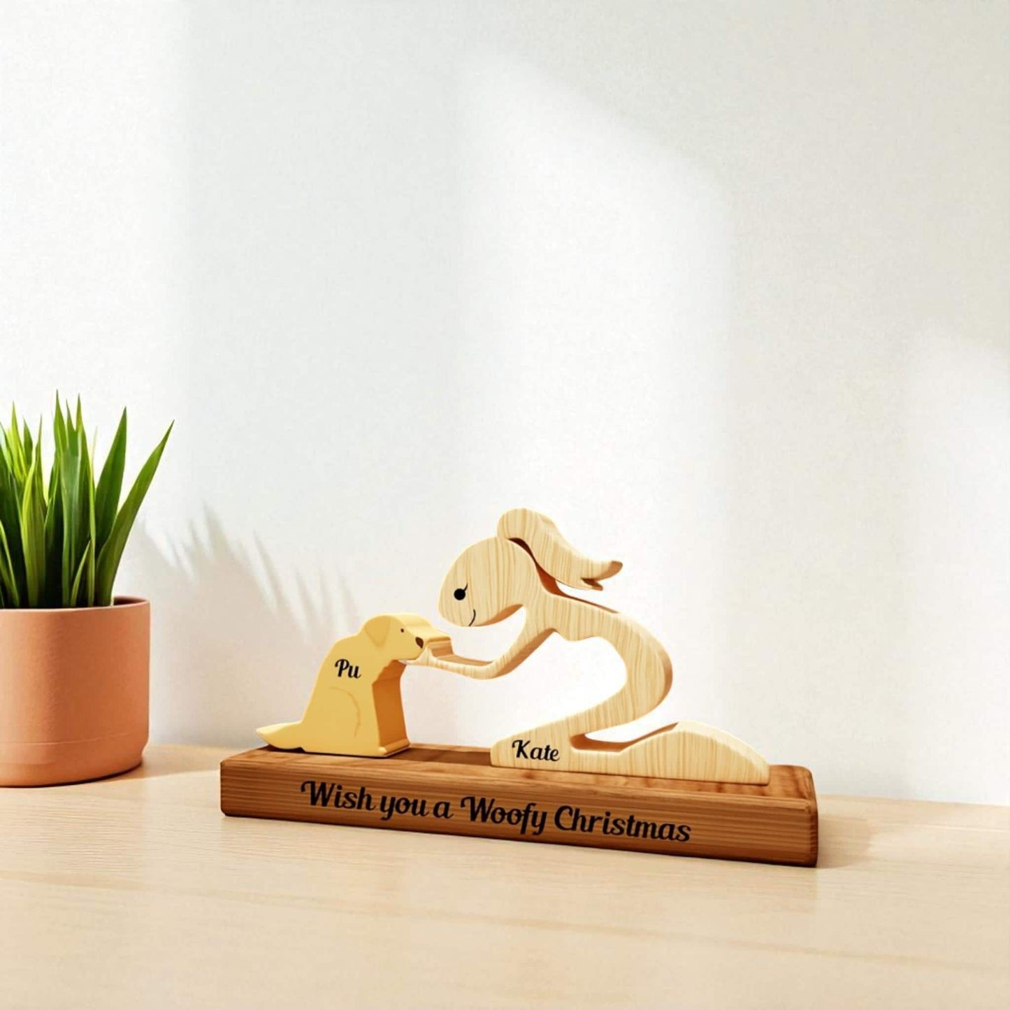 Wooden sculpture of a woman and a dog on a stand with 'Wish you a Woofy Christmas' text, next to a plant.