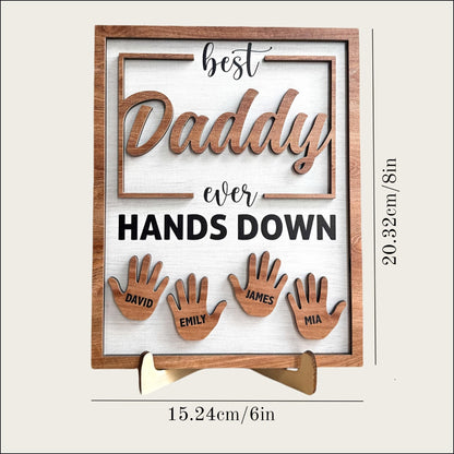Wooden plaque with cut-out letters spelling 'best Daddy ever HANDS DOWN' and cut-out hand shapes with names below on a white background.