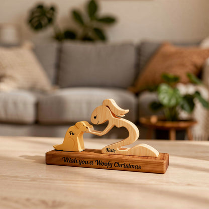Wooden sculpture of a woman and a dog on a stand with 'Wish you a Woofy Christmas' text, next to a plant.