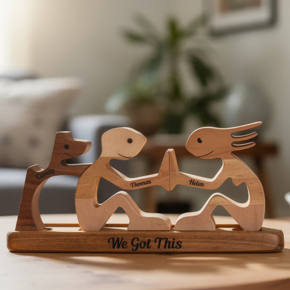 Wooden sculpture of a couple holding hands and their dog with engraved names and 'We Got This' text, placed on a surface, and their names engraved on each figurine. 