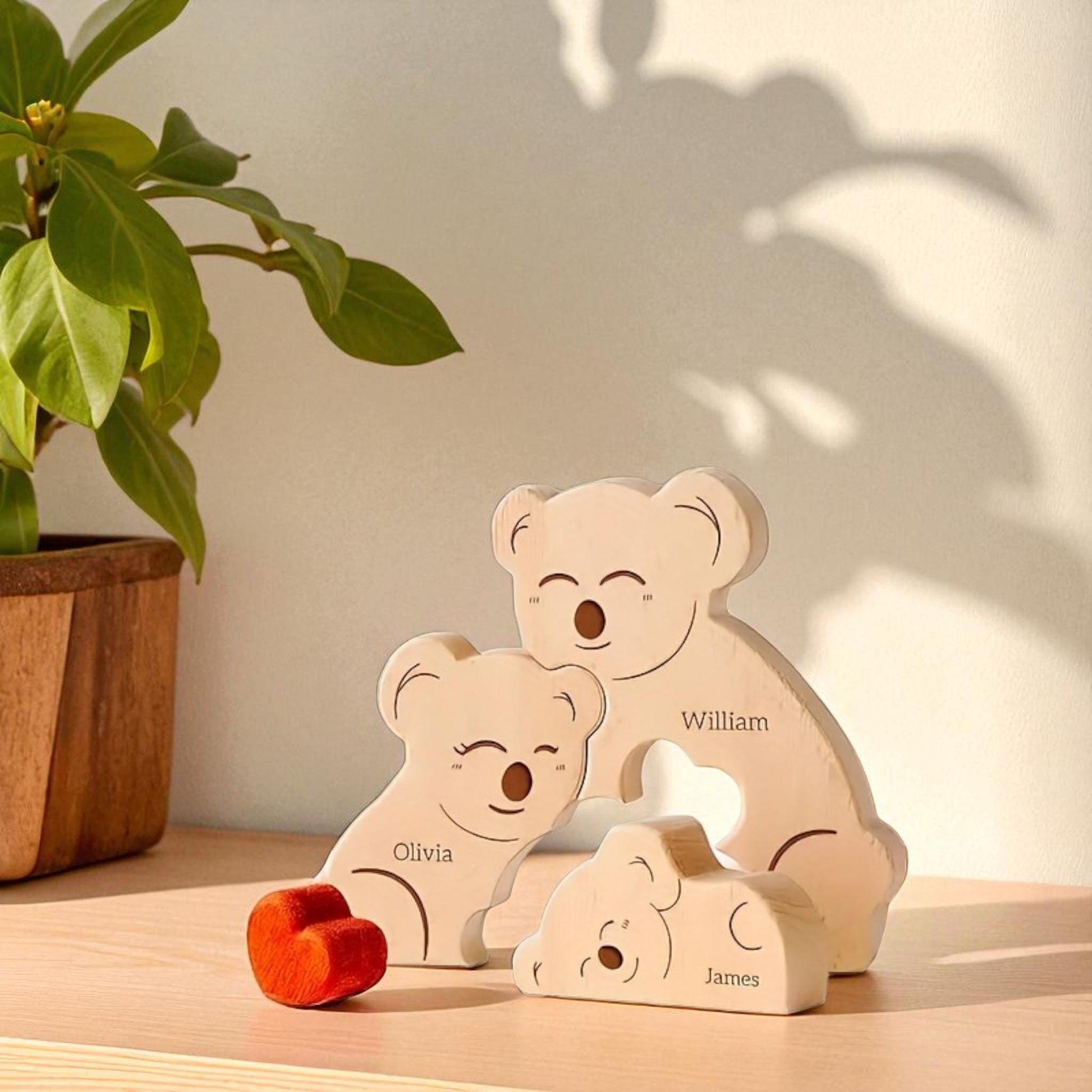 Handmade koala family ornament for trio of family members with engraving with a plant in the background.
