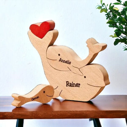 Handmade whale family keepsake showing family of three with engraving, on a wooden surface with a plant in the background.