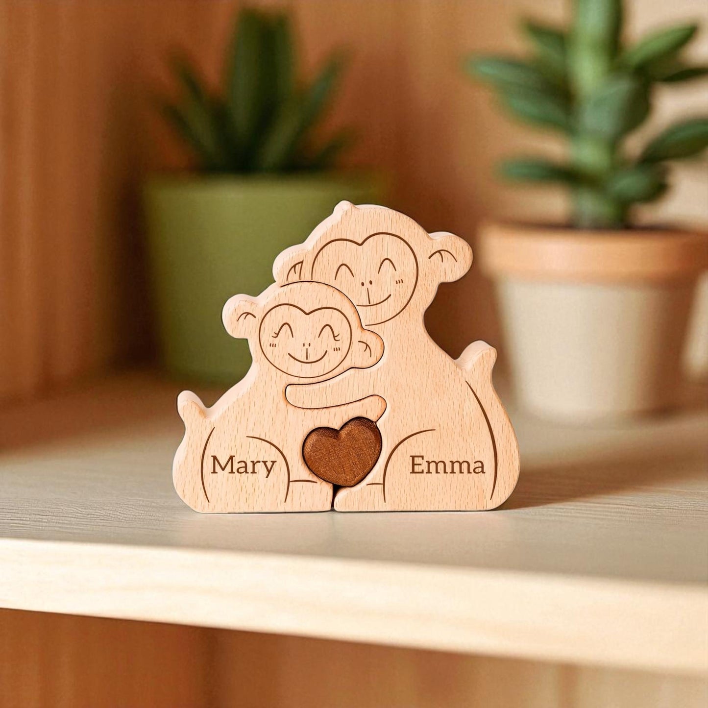 Wooden figurine of two monkeys holding a heart with engraved names, placed on a wooden surface with plants in the background.
