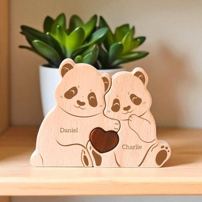 Two wooden panda bears holding a heart with engraved names on a wooden surface.