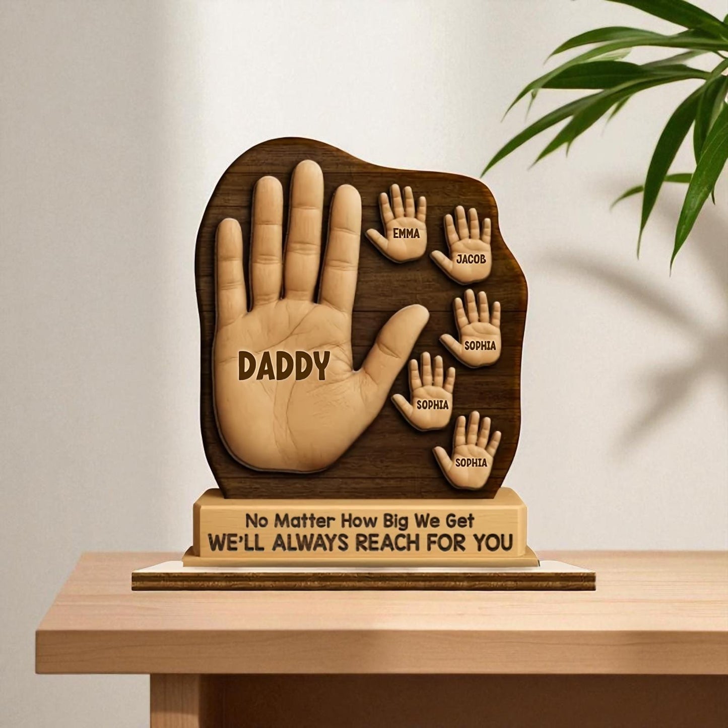 Wooden sculpture of a hand with engraved names on a stand, placed on a table.