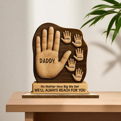Wooden sculpture of a hand with engraved names on a stand, placed on a table.