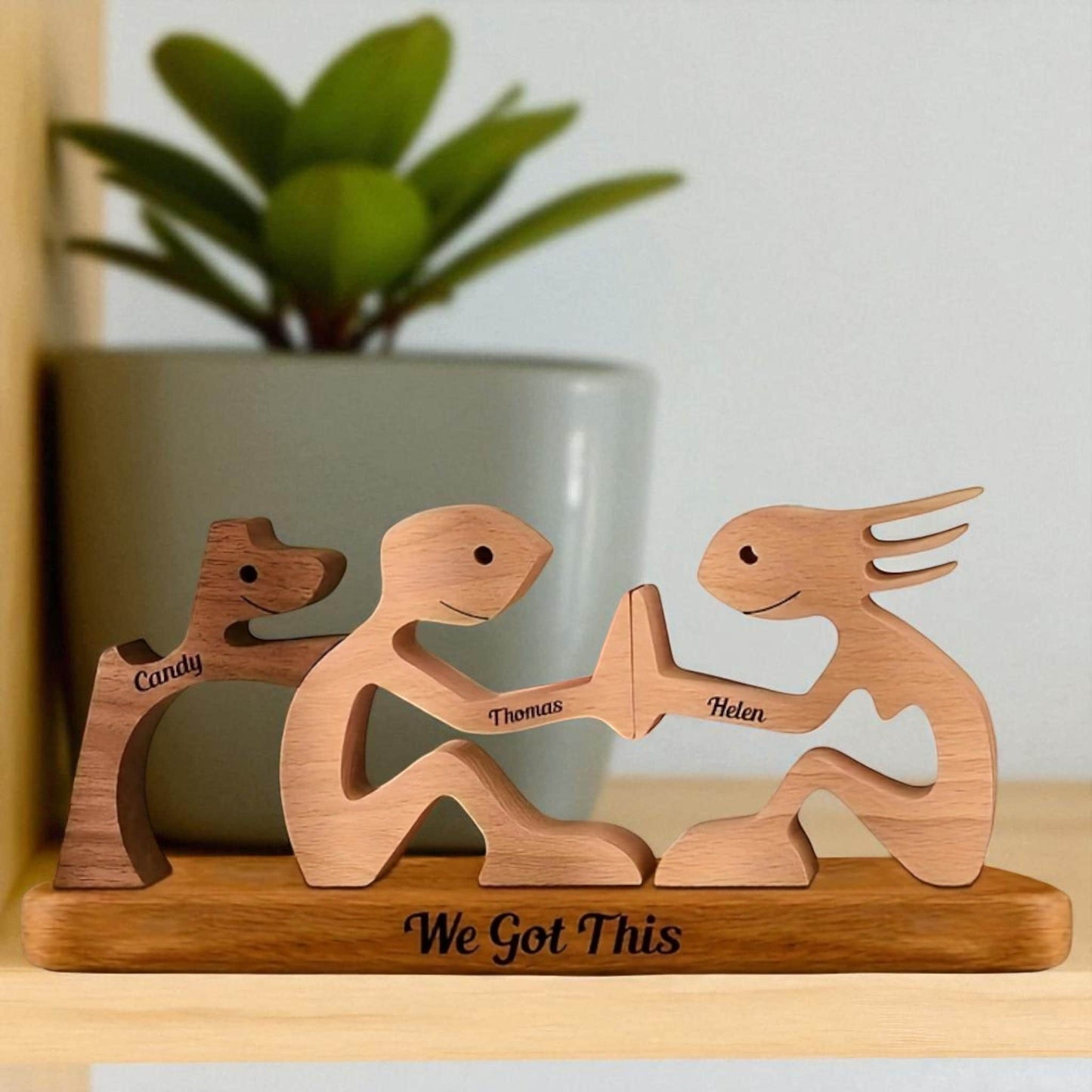 Wooden figurines of two people holding hands and a dog with engraved names and 'We Got This' text, placed on a wooden base.