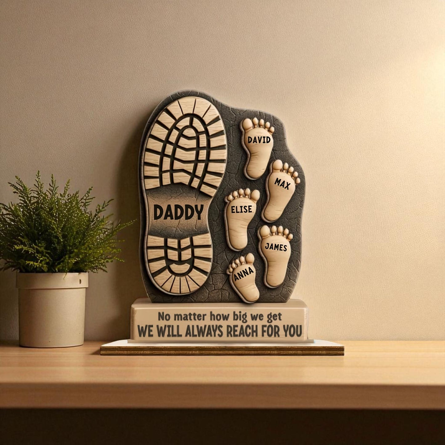 Wooden plaque with footprints and engraved names on a table with a plant in the background