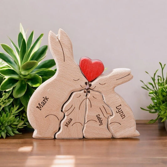 Wooden puzzle sculpture of four rabbits holding a heart with engraved names, placed on a wooden surface with plants in the background.
