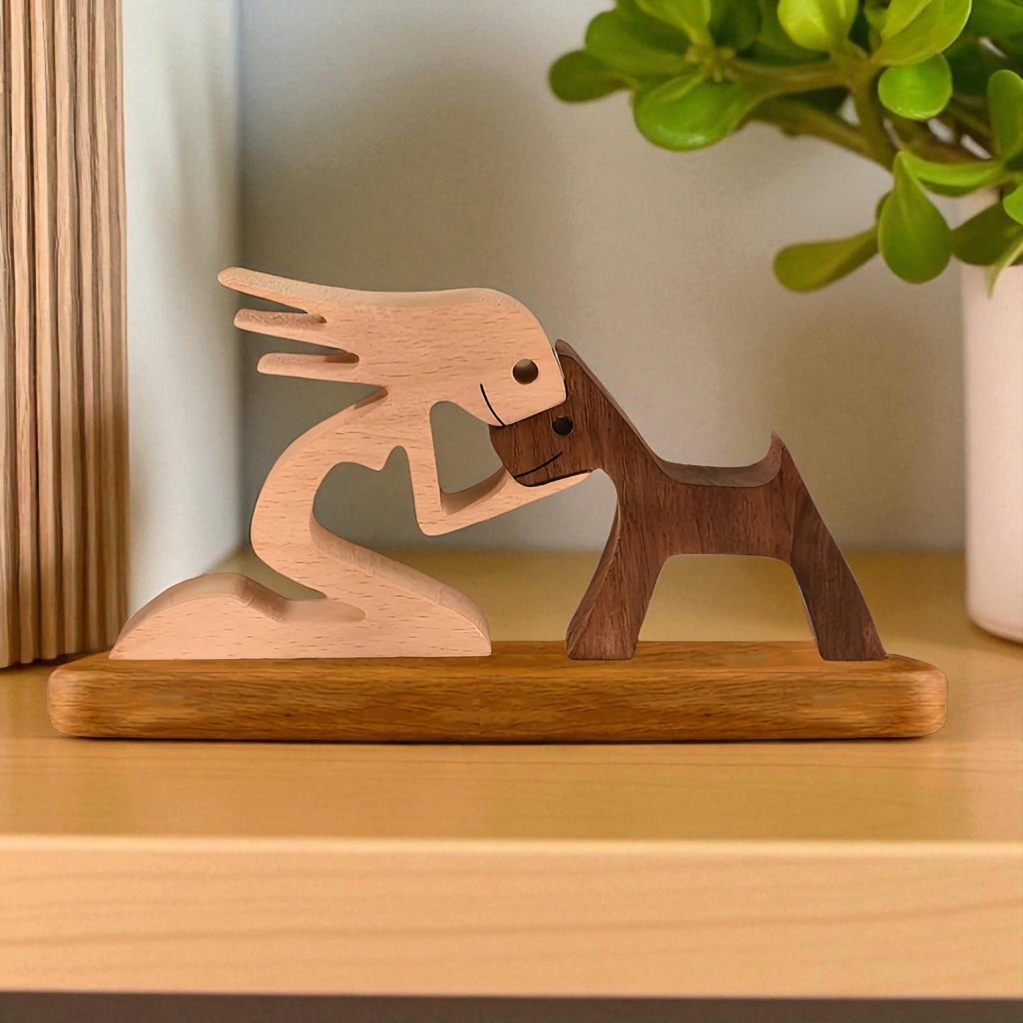 Wooden sculpture of a woman and a dog on a wooden base with a plant in the background.