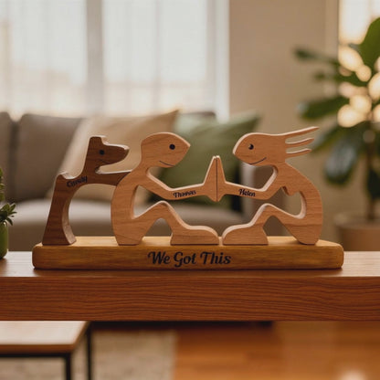 Wooden figurines of two people holding hands and a dog with engraved names and 'We Got This' text, placed on a wooden base.