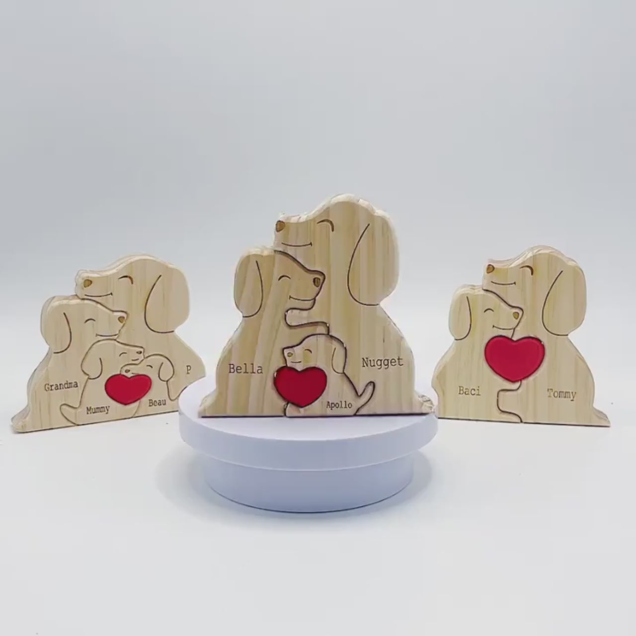 Wooden family puzzle of dog figurines with four pieces and a red heart, standing on a table with plants in the background.
